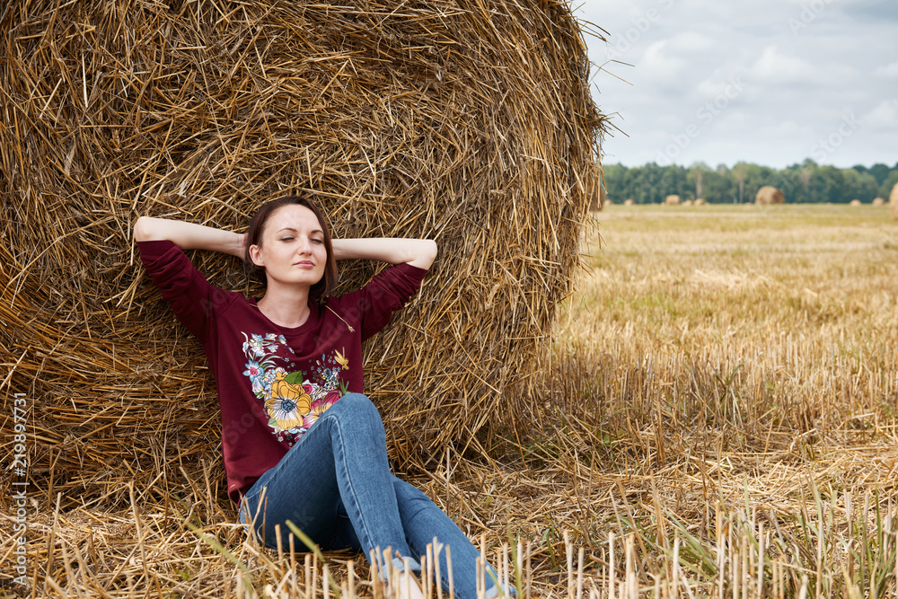 young girl having fun in the field, sits in a haystack and relaxing young girl having fun in the field, sits in a haystack and relaxing