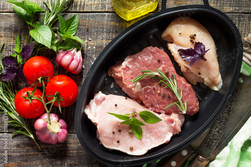Fresh raw meat. Different types of raw pork meat, chicken fillet and beef with vegetables and herbs on wooden table. Top view flat lay background.
