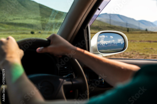 driving car on the mountain road. Guy inside the car driving on the country roadway between fields with brown grass and snowy mountains . Sun is shining. Shoot from the back.