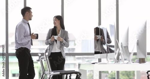 Businessman and businesswoman standing and drinking coffee while talking in modern office
