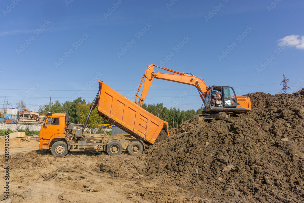 Orange excavator loads the land on a construction site.. Orange excavator loads the land on a construction site..