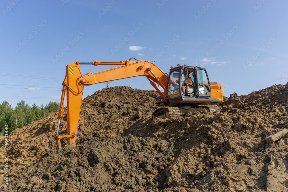Orange excavator loads the land on a construction site.. Orange excavator loads the land on a construction site..