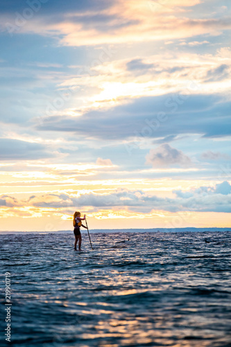 Beautiful woman stand up paddle boarding at sunrise or sunset