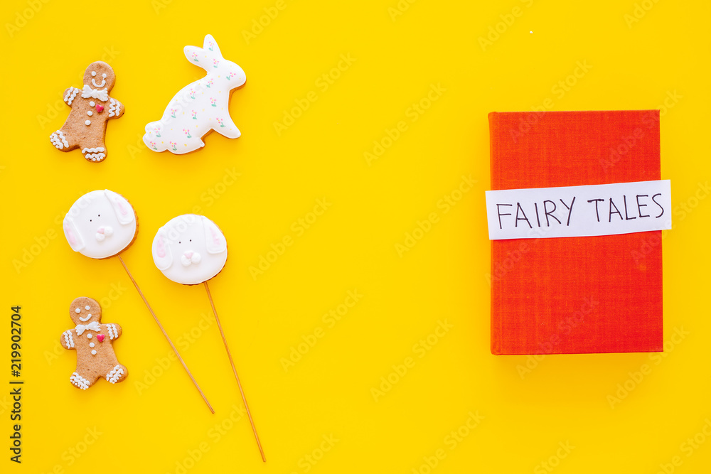 Fototapeta premium Fairy tales book near gingerbread man and candies on yellow background top view space for text