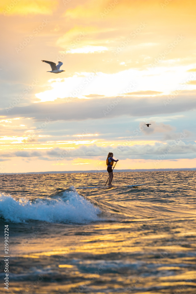 Beautiful woman stand up paddle boarding at sunrise or sunset