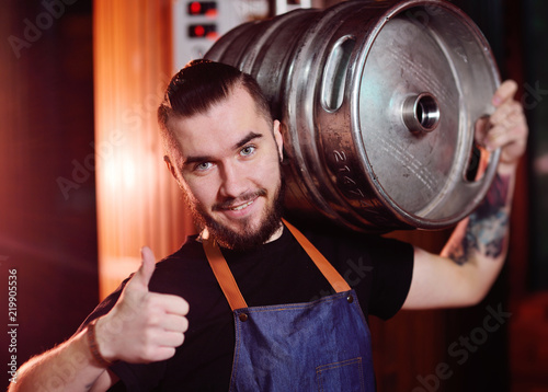 Cuadro en lienzo A bearded brewer in an apron holds a metal keg with beer in his hands and smiles