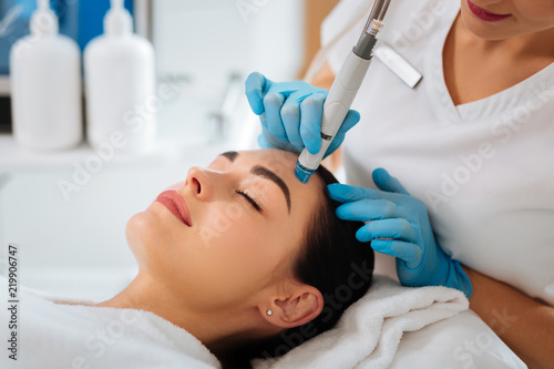 Professional cosmetology. Smart skilled cosmetologist using a modern device while doing hydrafacial procedure photo