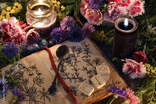 Still life with old book with botanical drawings, black candles, flowers and ritual objects. Mystic background with ritual esoteric objects, occult, fortune telling and halloween concept