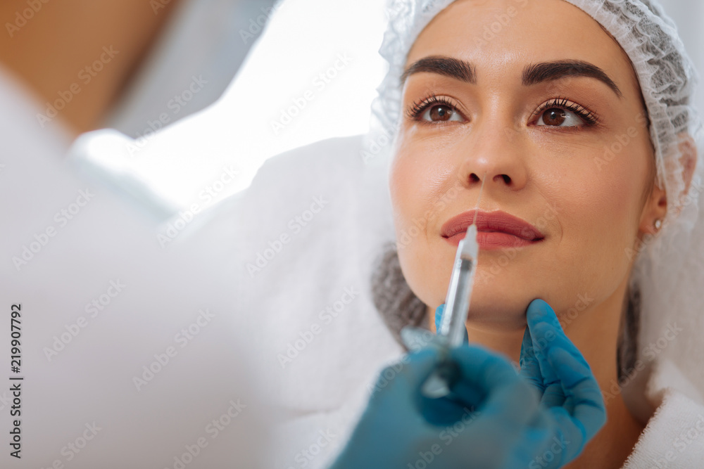 Will it hurt. Nice pleasant woman looking at her cosmetologist while waiting for an injection Will it hurt. Nice pleasant woman looking at her cosmetologist while waiting for an injection