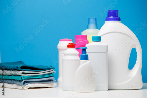 Photo of different bottles of cleaning products and colored towels isolated on blue background photo