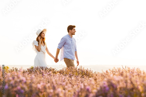 Cute loving couple walking in the lavender field outdoors holding hands of each other.