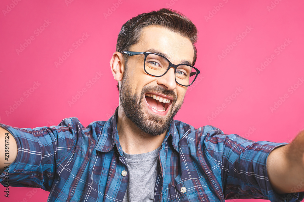 Obraz premium Portrait of a happy young man taking a selfie photo isolated over pink background. Close-up.