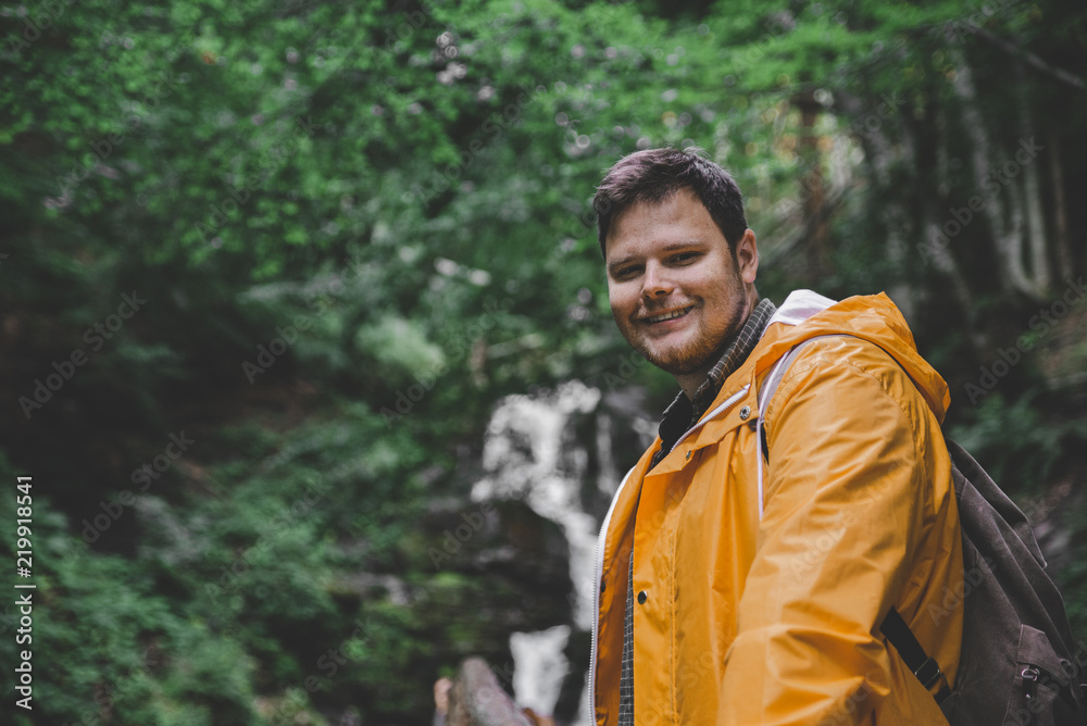 man walking by forest trail to waterfall in yellow raincoat