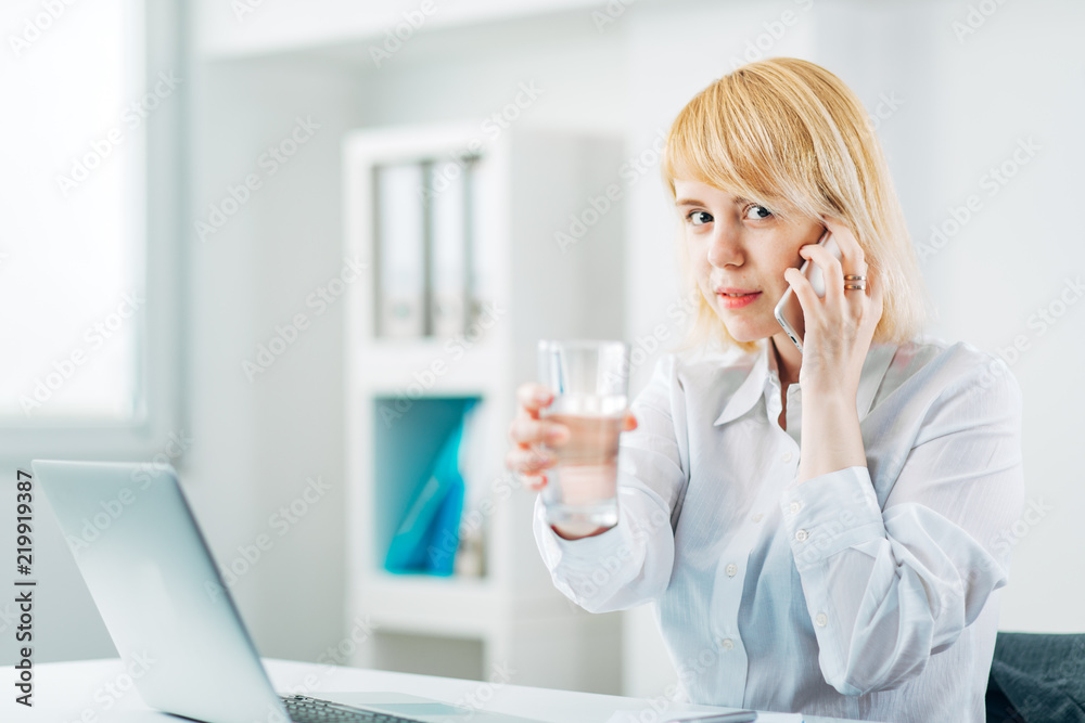 Woman Manager at the Office receiving good news on the phone and holding a glass of water Woman Manager at the Office receiving good news on the phone and holding a glass of water