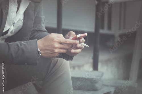 business man sitting and text sms message on mobile phone and smoking cigarette in hand at outdoor background