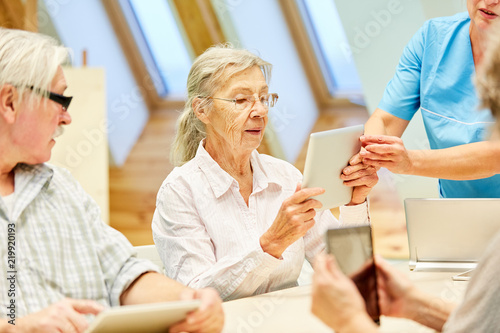 Pflegekraft hilft einer Seniorin mit Tablet PC
