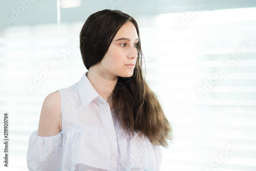 a girl in a white shirt and with her hair down is standing near the window