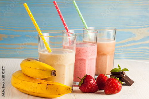 Long glasses of milkshakes with chocolate, strawberry, banana, with ice cream on white and blue background. Shakes and smoothies. Milk shake and cocktail for summer.
