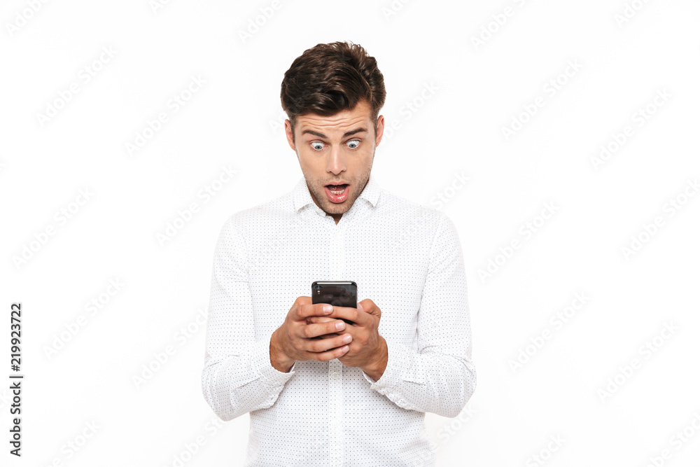Surprised man with short dark hair chatting or typing text message using cell phone, isolated over white background Surprised man with short dark hair chatting or typing text message using cell phone, isolated over white background