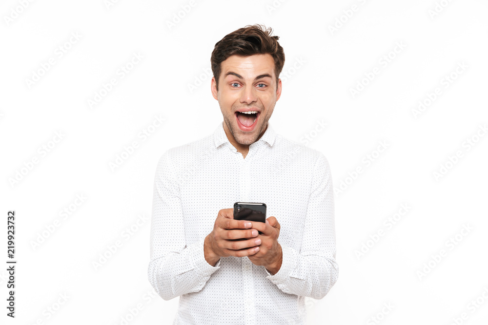 Cheerful guy with short dark hair chatting or typing text message using mobile phone, isolated over white background Cheerful guy with short dark hair chatting or typing text message using mobile phone, isolated over white background