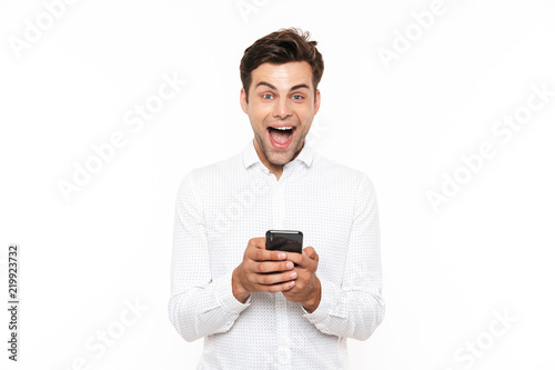 Cheerful guy with short dark hair chatting or typing text message using mobile phone, isolated over white background © Drobot Dean