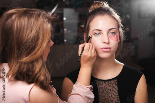 makeup woman applying a make up on a young model wearing hydrogel treating eye patches. concept of professional skin care
