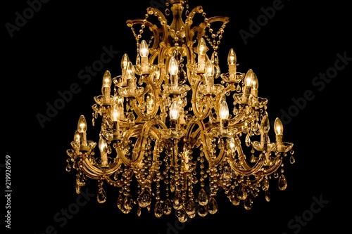 Luxury interior chandelier has light candles and dark background. Noble candelabra hanging on ceiling with lots of little gems. Premium decoration for palace gala, villa business meeting or wedding