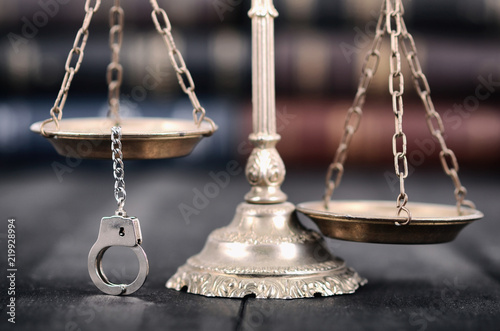 Scales of Justice and handcuffs on a black wooden background.
