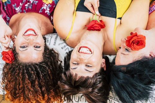 playful group of young females friends at home together laughing and smiling. lay down on bed and taken from aerial view. make up beauty perfect to go out and rose for each one. beautyness concept photo