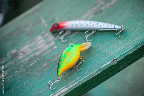 Old plastic spinning bait on rustic, green wooden background. Fishing equipment. Fishing lures with big hooks.  
