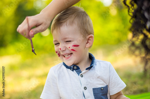 Mother and son paint their face outdoor. Concept of happy family photo