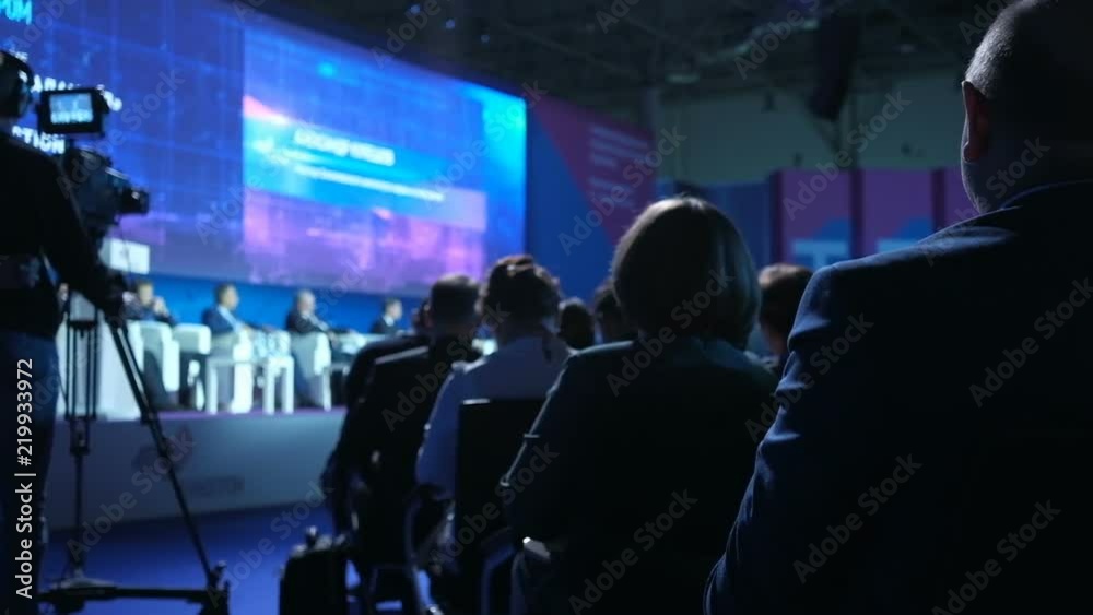 People on the forum on business development. The audience. Hall is full. Audience listens to the speech in the conference hall. International economic business forum. Back view. People on the forum on business development. The audience. Hall is full. Audience listens to the speech in the conference hall. International economic business forum. Back view.