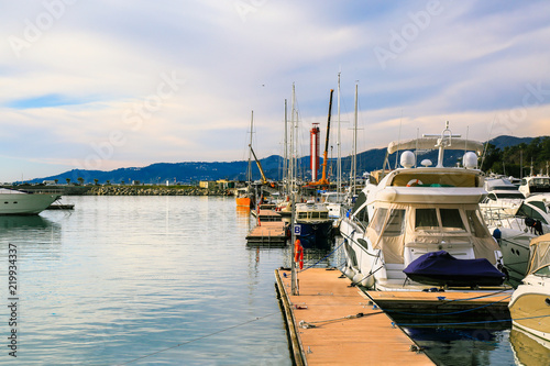 Luxury yachts moored at pier in sea port at sunset, back view. Marine dock of modern motor and sailing boats, blue water sea. Travel and fashionable vacation.