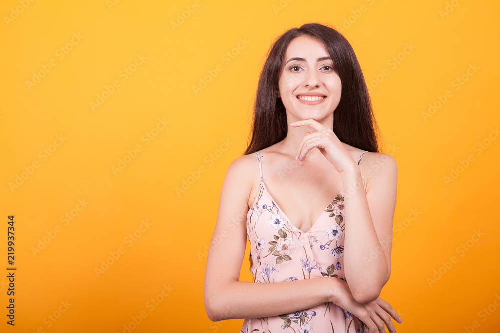 Attractive young woman smilling at the camera in studio over yellow background in short dress. Attractive young woman smilling at the camera in studio over yellow background in short dress.