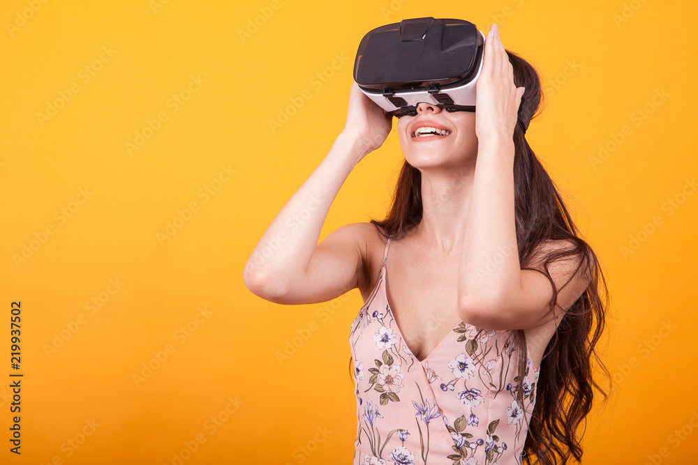 Happy beautiful girl wearing virtual reality goggles in studio over yellow background. VR 360 gaming technology.