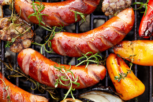 Grilled sausages and vegetables with addition spices and fresh herbs on a grill plate, top view