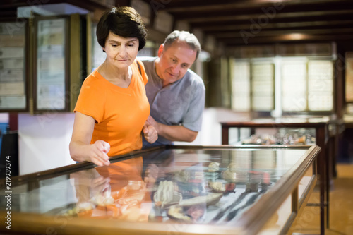 Two visitors are looking at the exposition under glass in historical museum.