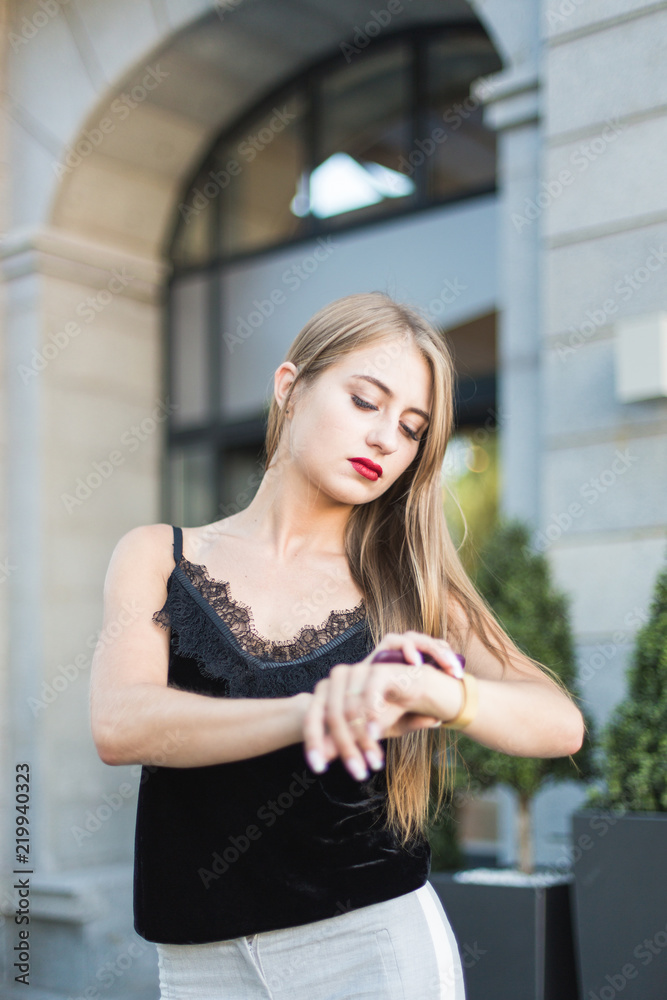 beautiful young business woman on the street waiting for a meeting with the client. looks at the clock, late