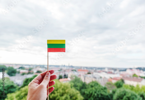 A small Lithuanian paper flag in a woman's hand against a background of a blurred city, the capital of Lithuania Vilnius, welcome to Lithuania