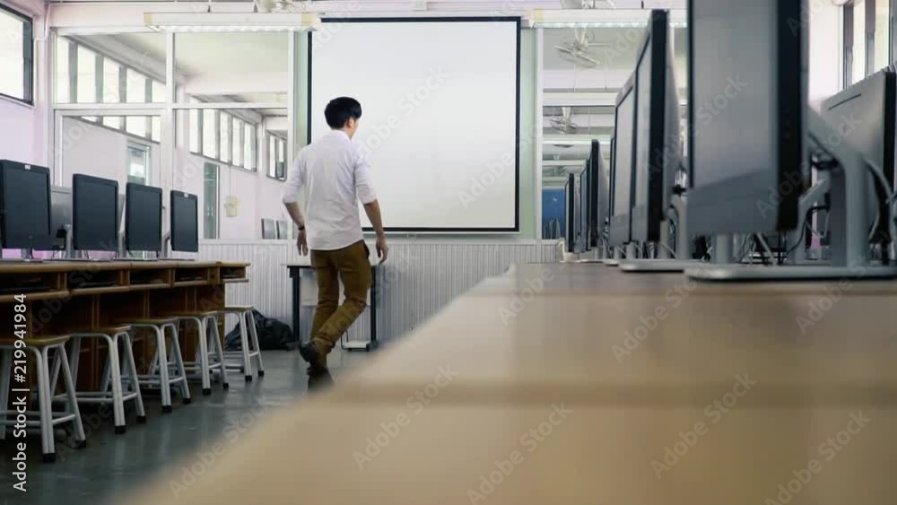 Young Asian male technician checking computers in computer laboratory room before seminar, class session starts Young Asian male technician checking computers in computer laboratory room before seminar, class session starts