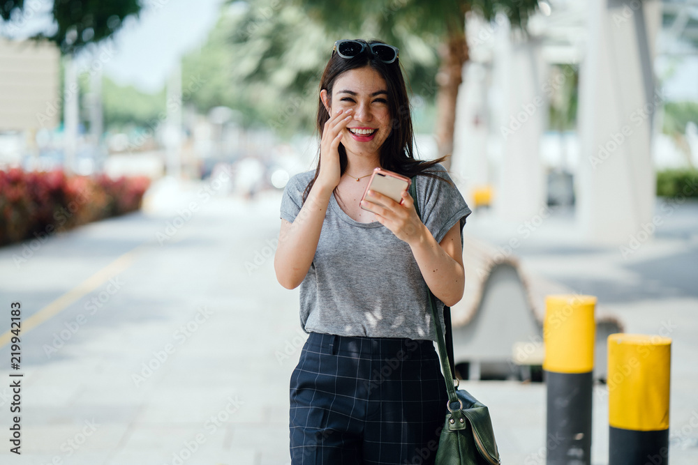 Fototapeta premium Portrait of a Japanese Asian woman tourist in the streets in Singapore. She is young, attractive and is wearing comfortable and casual clothes as she wanders the sunny streets.
