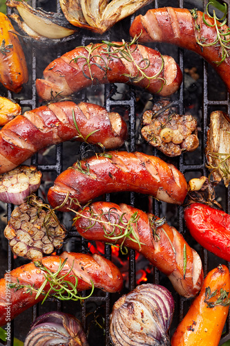 Grilled sausages and vegetables with addition spices and fresh herbs on a grill plate, top view