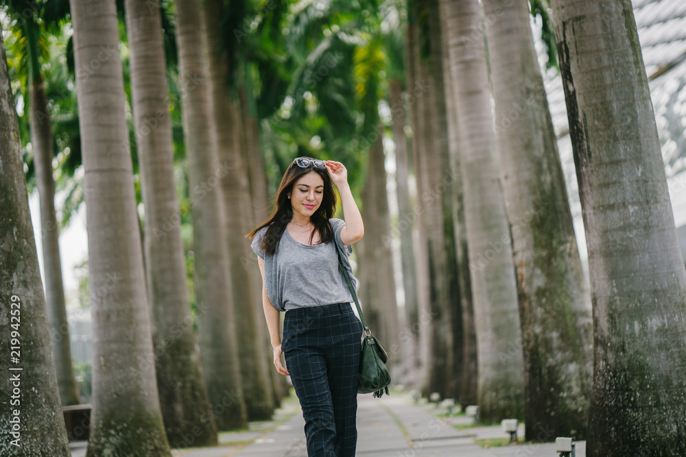 A young Japanese Asian woman is walking at the park on a hot sunny day. She is enjoying her time and smiles comfortably. A young Japanese Asian woman is walking at the park on a hot sunny day. She is enjoying her time and smiles comfortably.