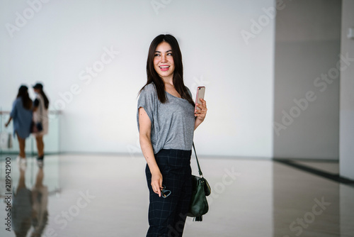 Portrait of a young Japanese Asian woman holding her smartphone and walking in a clean, modern and futuristic mall. She is comfortably dressed in loose clothing with a sling bag. photo