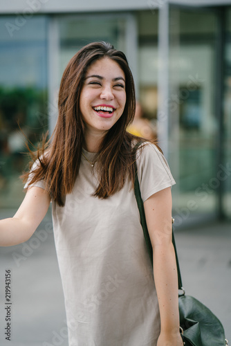 A young attractive Japanese tourist poses in a park during the day. She is pretty and smiling happily for her photograph.