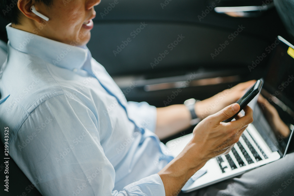 Portrait of a young Japanese man getting some work done while inside the car. He is being driven to his destination in a ride he booked on a ride hailing app. Portrait of a young Japanese man getting some work done while inside the car. He is being driven to his destination in a ride he booked on a ride hailing app.