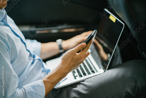 Portrait of a young Japanese man getting some work done while inside the car. He is being driven to his destination in a ride he booked on a ride hailing app.  © Danon
