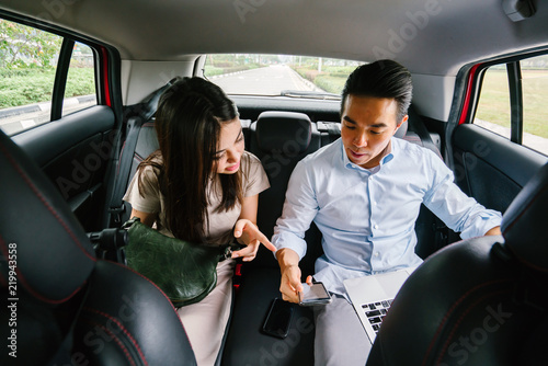 A young Japanese couple area seated at the backseat of a car. They are having a fun-filled discussion about what they are planning to do when they reach their destination. photo