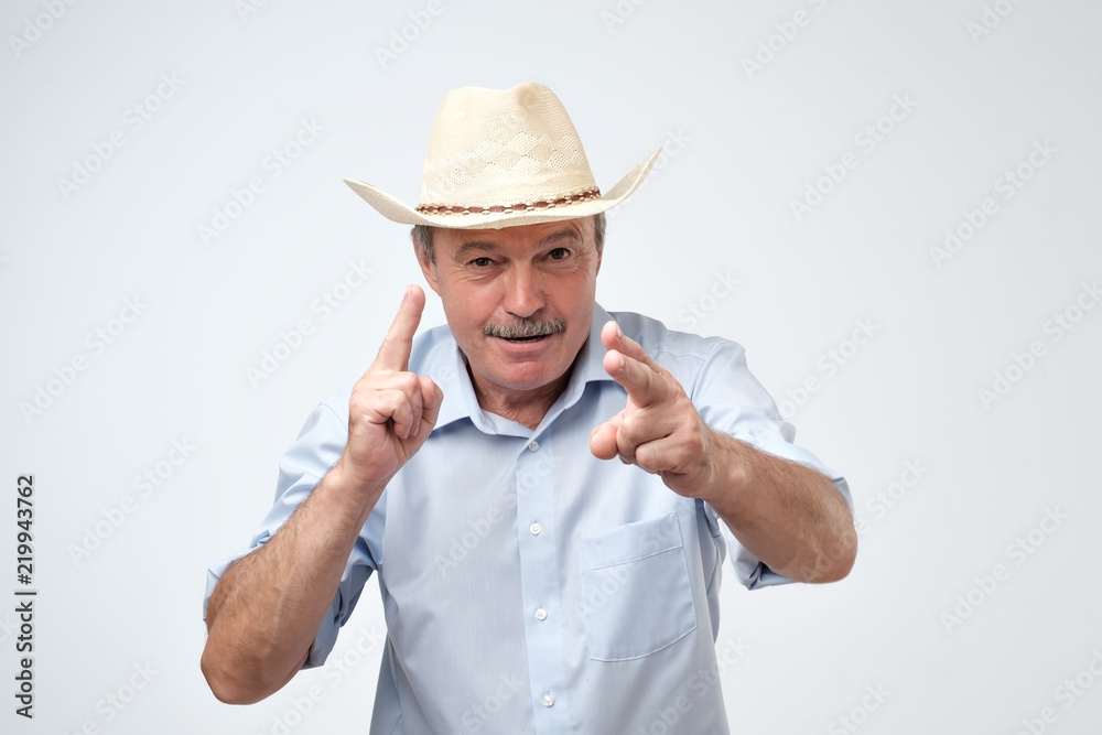 Mature caucasian man in cowboy hat making a sign with fingers like he is shooting ahead. Mature caucasian man in cowboy hat making a sign with fingers like he is shooting ahead.