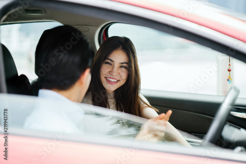 A young attractive Japanese couple are going on a trip in a red car. Both of them look happy and excited to reach their destination.
